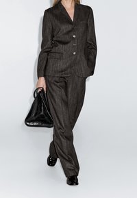 Costume à fines rayures sombres confectionné dans un tissu texturé, doté d'un col à revers cranté, d'une fermeture à deux boutons, et d'un pantalon assorti. Accompagné d'un sac triangulaire noir.