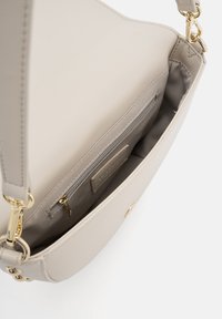 Sac à main en cuir beige clair avec une texture lisse, doté d'une poche zippée et de quincaillerie dorée. Intérieur ouvert visible.