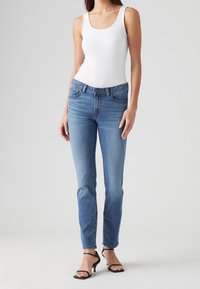Ljust blå denimjeans med rak passform, fem fickor och knappstängning, kombinerat med en åtsittande vit linne.