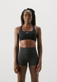 Svart sports-bh og høyde shorts laget av elastisk materiale. Bh-en har firkantet halslinje og logo; shortsene har en tettsittende design.