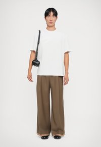 Witte t-shirt met korte mouwen, bruine wijde broek, zwarte schoudertas en zwarte schoenen. Gladde stof, ontspannen pasvorm, eenvoudig ontwerp.