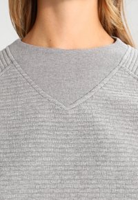 Sweatshirt gris avec un design côtelé texturé, doté d'un col en V et d'accents de coutures légèrement surélevées sur les épaules.
