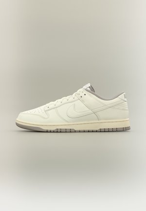 Pantof sport tip low-top Nike din piele albă-crem cu vârf perforat, închidere cu șiret și talpă de cauciuc gri, prezentat în profil lateral.