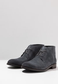 Bottines en daim gris avec un bout rond, un design à lacets et un petit talon empilé. Texture lisse et détails de couture minimaux.