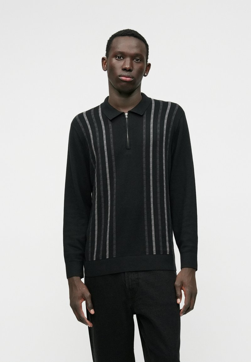 Μαύρο πουκάμισο με μακριά μανίκια και μισό φερμουάρ. Διαθέτει κατακόρυφες γκρίζες ρίγες, γιακά και ριγωτό στρίφωμα. Κατασκευασμένο από υφασμάτινη υφή.