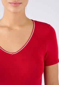 Rode katoenen t-shirt met een v-hals ontwerp, voorzien van een smalle witte rand langs de halslijn en korte mouwen. Soepele textuur, getailleerde vorm.