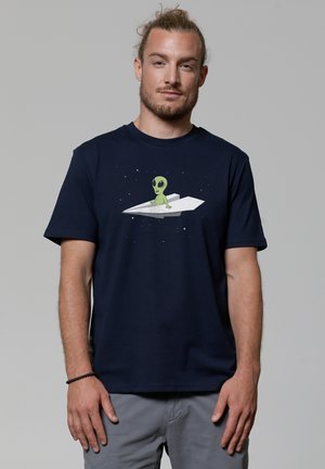 Navy t-shirt featuring a green alien character on a paper airplane, with a starry background. Short sleeves and round neckline.