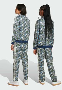 Futrová súprava s kvetinovým potlačou v námorníckej modrej a zelenej farbe, s bielymi pruhmi na rukávoch a nohaviciach. Elastický materiál s rebrovanými manžetami a pásom.