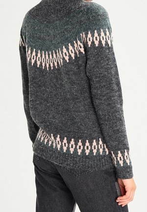 Ciemnoszary sweter z jasnoróżowymi geometrycznymi wzorami na górnej części pleców, w talii i mankietach, noszony przez osobę w czarnych dżinsach.