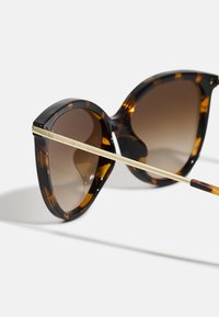 Ochelari de soare din tortoise, cu formă oversized tip cat-eye. Lentile maro cu gradient și accente din metal aurit pe brațele subțiri.