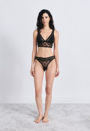 Ensemble de lingerie en dentelle noire comprenant un bralette à col en V et un string assorti, mettant en valeur des motifs floraux et des détails en tissu transparent.