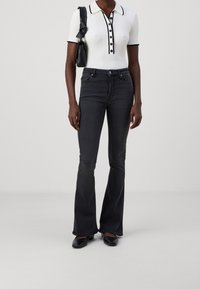 Black flared jeans paired with a white ribbed polo shirt featuring a black collar and buttons, complemented by black footwear and a small bag.