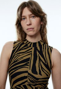 Ärmelloses Oberteil mit hohem Kragen, das ein gelb-schwarzes Zebra-Streifenmuster aufweist. Hergestellt aus strukturiertem Rippstoff mit enger Passform.