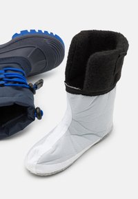 Bota alta impermeable con una suela de goma azul y negra, caño de tela gris y un suave forro de felpa negra con una abertura ajustada.