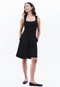 Zwarte mouwloze top met een vierkante halslijn, gecombineerd met zwarte hoge taille shorts met zijzakken en een ontspannen pasvorm. Zwarte ballerina's gedragen.