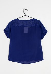 Námořnicky modrá blůza s vyšívanou krajkovou vrstvou na ramenou, krátkými rukávy, volným střihem a zakřiveným lemem. Vyrobena z lehkého, průsvitného materiálu.