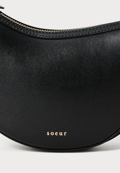 Crna kožna torba s zakrivljenim dizajnom, koja se ističe glatkom teksturom i zlatnim hardverom. Logotip "Soeur" ugraviran je na prednjoj strani.