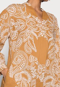 Langærmet skjorte i brændt orange med hvide blomster- og paisley-mønstre. Letvægtsstof med en afslappet krave og silhuet.