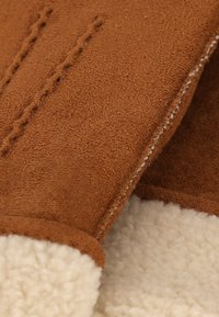 Bruine suède handschoenen met een zachte crème voering, opvallende stiksels langs de naden en een gladde textuur. Warme en duurzame uitvoering.