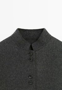 Ciemnoszara wełniana kurtka z kołnierzem w stylu mandarynki i czterema czarnymi guzikami ułożonymi pionowo.