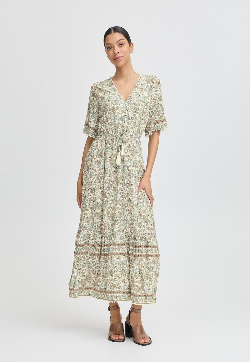 Robe maxi avec un décolleté en V, manches courtes, motif cachemire dans des couleurs atténuées, et une taille élastique. Présente des accents en dentelle et une jupe évasée.