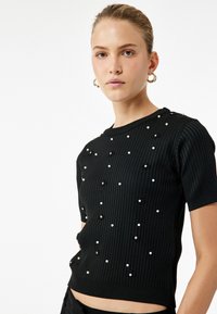 Sort ribbet kortærmet sweater prydet med perle- og palietdetaljer. Har en rund hals og en tætsiddende silhuet.