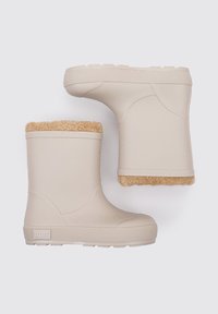 Botas de goma beige con un suave forro de piel sintética en la parte superior, con suela texturizada y diseño curvado. Logotipo de la marca visible en el lateral.