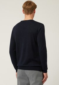 Maglione pullover blu navy con maniche lunghe, scollatura rotonda e polsini a coste. Texture morbida, design minimalista e senza motivi o loghi visibili.
