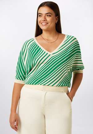 Gebreide top met groene en crèmekleurige strepen, V-hals en korte mouwen; gecombineerd met lichtgekleurde, wijd uitlopende broek. Zachte textuur, casual pasvorm.