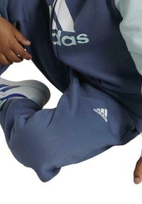 Chándal azul de Adidas que incluye un sudadera azul claro con un logo prominente, cintura elástica y pantalones ajustados con acento de logo.