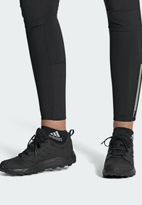 Leggings atléticos negros con costuras planas y un bolsillo con cremallera, combinados con zapatos ligeros negros que presentan una suela texturizada y un logotipo.