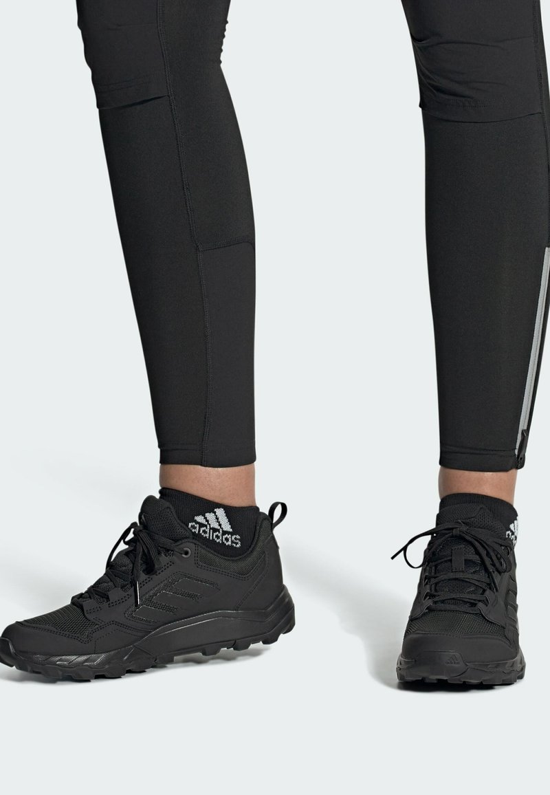 Leggings atléticos negros con costuras planas y un bolsillo con cremallera, combinados con zapatos ligeros negros que presentan una suela texturizada y un logotipo.