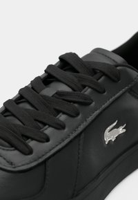 Μαύρο αθλητικό παπούτσι από δέρμα με επίπεδες μαύρες κορδόνες, λεία υφή και ασημί λογότυπο στο πλάι. Απλός σχεδιασμός, χαμηλή σιλουέτα.