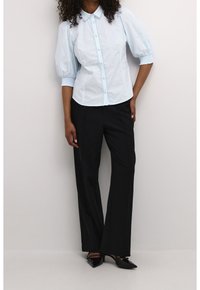 Light blue button-up shirt with puffed sleeves and a scalloped collar, paired with black straight-leg trousers and pointed black shoes.