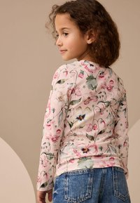 Cămașă cu mânecă lungă din țesătură ribată de culoare roz, cu modele florale multicolore. Asortată cu blugi din denim albastru.