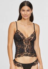 Must musträtik, millel on läbipaistvad paneelid, V-kaelus, reguleeritavad rihmad ja dekoratiivsed nööbid. Ääristatud pitsiga ja kontrastsete detailidega.