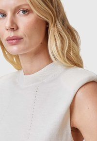 Witte mouwloze gebreide top met een hoge kraag, voorzien van subtiele verticale stikdetails aan de voorkant. Gladde textuur en een aansluitend ontwerp.