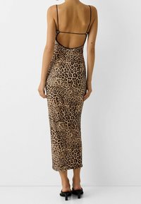 Midi šaty s leopardím potiskem, tenkými černými ramínky, otevřeným zadním dílem a jemnou texturou. Mají přiléhavý střih a délku ke kolenům.
