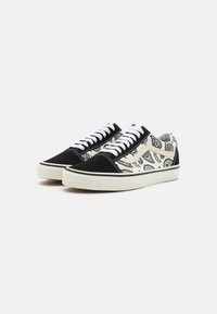 Svarte mockaskinn- og mønstrede tekstilsneakers med hvite lisser, gummisåle og dekorative øye-motiver i svart på hvit bakgrunn.