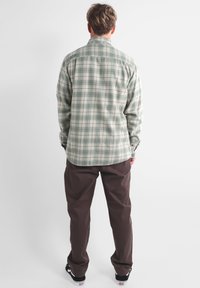 Chemise à manches longues à carreaux verts et beiges avec un col boutonné, en tissu coton, coupe droite, associée à un pantalon marron.
