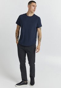 Námornícky modré bavlnené tričko s okrúhlym výstrihom, krátkymi rukávmi a zakriveným spodným lemom. Kombinované s čiernymi nohavicami a čiernymi teniskami.