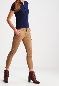 Marinblå pikétröja med korta ärmar, khakifärgade cargobyxor med flera fickor, samt bruna ankelstövlar med klack och flätade detaljer.