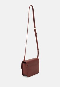 Lille struktureret mørkebrun crossbody-taske med en frontklap og justerbar skulderrem mod en hvid baggrund.