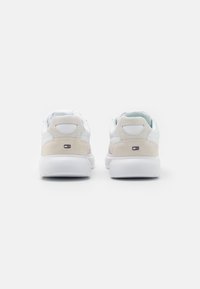 Sneaker bianche con una finitura in pelle liscia, accenti in suede beige, tacco imbottito e dettaglio del logo sul retro.
