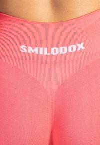 Rosa Leggings mit einem gerippten Bund, der den Markennamen "SMILODOX" in Weiß zeigt. Glatte Textur mit figurbetontem Design.
