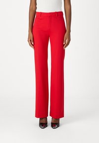 Røde, høytlivs, vide bukser i lett materiale med beltehemper. Kombinert med svarte spisse sko, som skaper et formelt utseende.