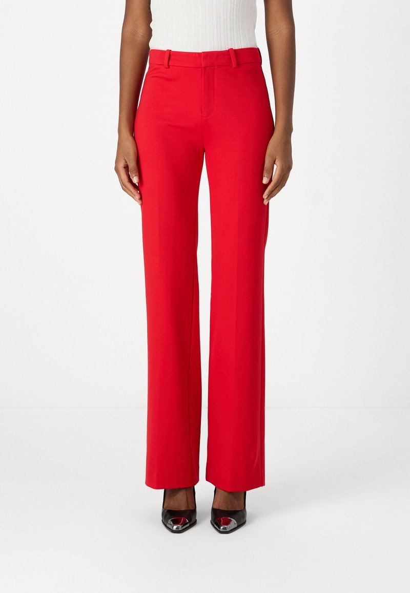 Røde, høytlivs, vide bukser i lett materiale med beltehemper. Kombinert med svarte spisse sko, som skaper et formelt utseende.