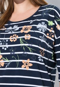 Mörkblårandig skjorta med vita horisontella ränder, med blommönster i orange, grönt och grått, med rund halsringning.