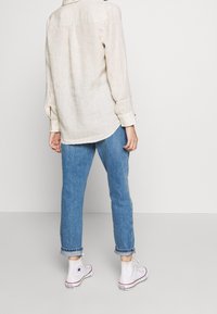 Beige liinakootud särk pikkade varrukatega, tagant õmmeldud yoke'iga ja nööpidega. Ühendatud helesiniste teksapükste, rullitud sääreotste ja valgete kõrgete tossudega.