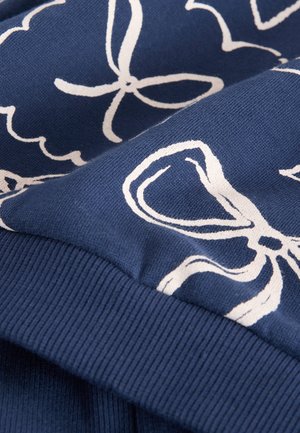 Meresvamariinist puuvillane kangas, millel on valged lille- ja paelaprindid; soonikviimistlus allservas lisab tekstuuri. Lähedalt võetud vaade kujunduse detailidele.